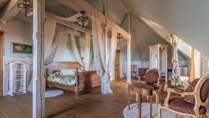 A bedroom with a four-poster bed, a sitting area with a table and chairs, and a view of the kitchen. - Mazmežotnes muiža (Mazmežotne)