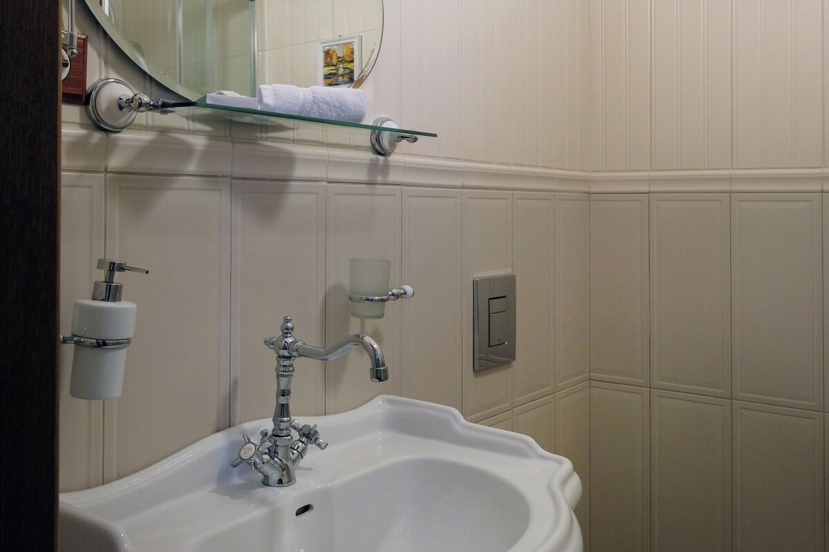 A bathroom with a white sink, a toilet, a mirror, and a glass shelf.