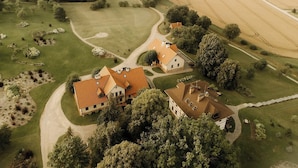 An aerial view of a rural property with a large house, expansive fields, and a river. - Mazmežotnes muiža (Mazmežotne)