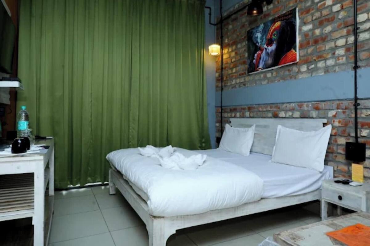 A bedroom with a bed, a nightstand, a lamp, a water bottle, and a brick wall with a painting.