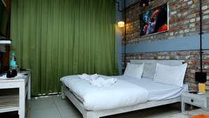 Un dormitorio con una cama, cortinas verdes, una pared de ladrillo y un cuadro.