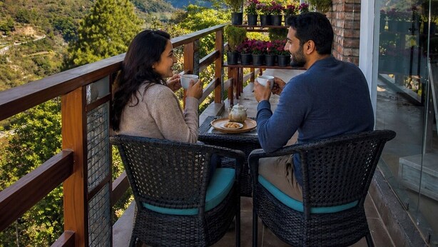 Un balcón con vistas a montañas nevadas, sillas de mimbre y una mesa con tetera y tazas.