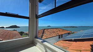 Blick aus einem Fenster auf eine Küstenlandschaft mit Terrakotta-Dächern und Solaranlagen.