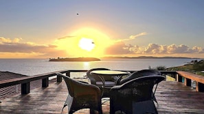 A wooden deck with chairs and a table overlooking a sunset over the sea. - House with ocean view, resort-style beachfront condominium. (Armação dos Búzios)