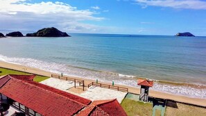 Blick auf die Küste mit Strand, einer Holzpromenade und einem kleinen Gebäude mit rotem Dach.