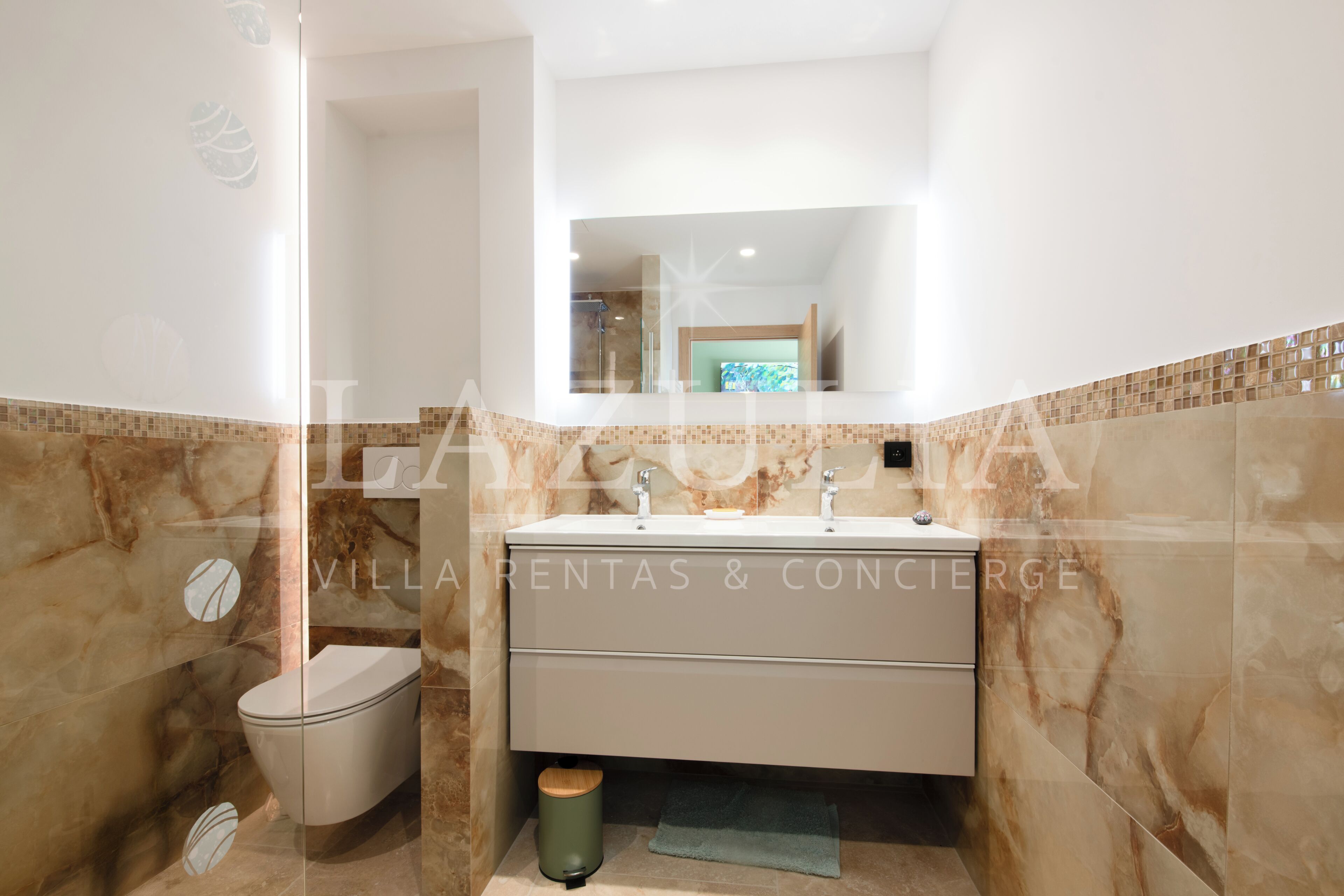 A bathroom with a marble wall, a sink, and a toilet.