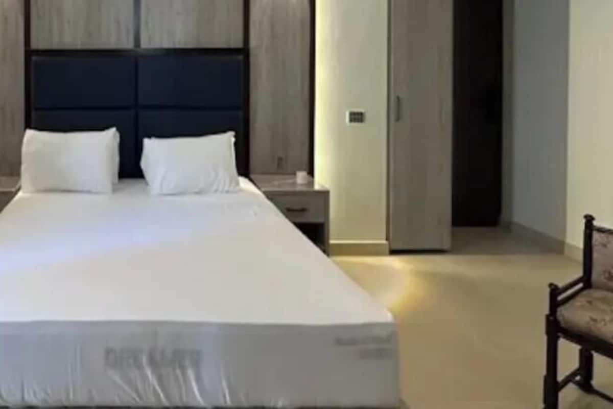 A hotel room with a large bed, a wooden headboard, a nightstand, and a chair.