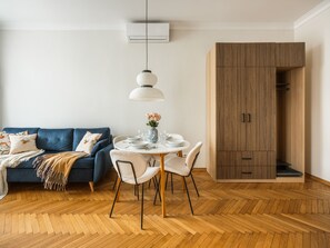 Een moderne woonkamer met een blauwe bank, een eettafel met stoelen, een hanglamp en een houten garderobe.