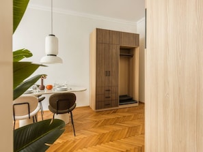 A modern room with a wooden floor, a dining table with chairs, a hanging light fixture, and a wardrobe with a sliding door. - Florian Gate by Fragola Collection (Kraków)
