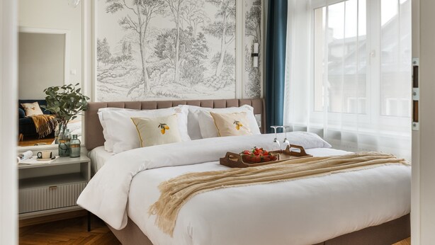 A bedroom with a large bed, a nightstand, a dresser, and a wall with a tree mural. - Florian Gate by Fragola Collection (Kraków)