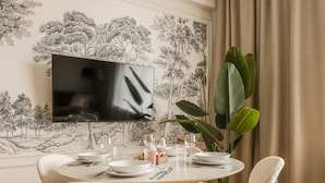 A dining area with a round table, chairs, a TV mounted on the wall, and a large plant. - Florian Gate by Fragola Collection (Kraków)