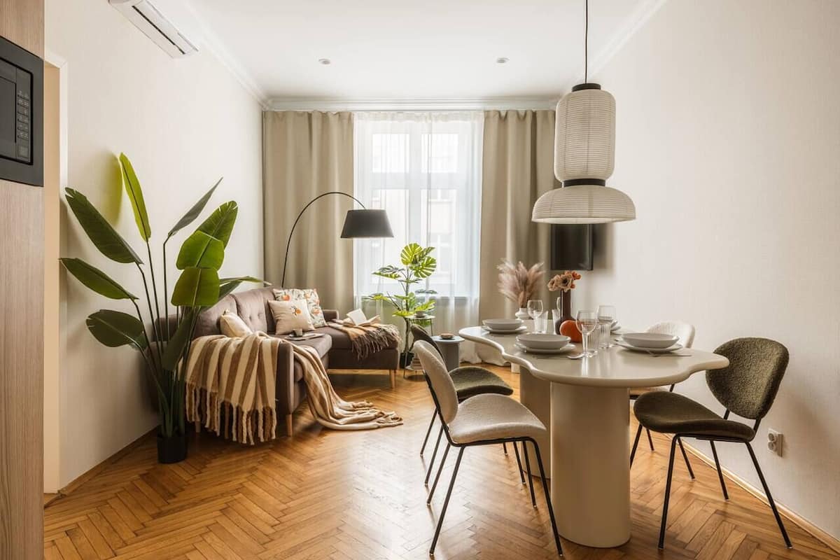 A modern living room with a sofa, dining table, chairs, and a large plant.