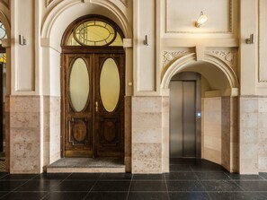 A grand entrance with a double wooden door, an elevator, and a light fixture above. - Florian Gate by Fragola Collection (Kraków)