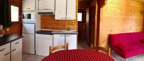 A compact kitchen with a sink, microwave, and stove, a dining table with a red tablecloth, and a bright red sofa.