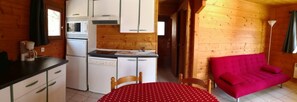 A compact kitchen with a sink, microwave, and stove, a dining table with a red tablecloth, and a bright red sofa. - In the Périgord Noir, between Sarlat and Montignac, comfortable chalet* in a peaceful setting (Saint-Geniès)