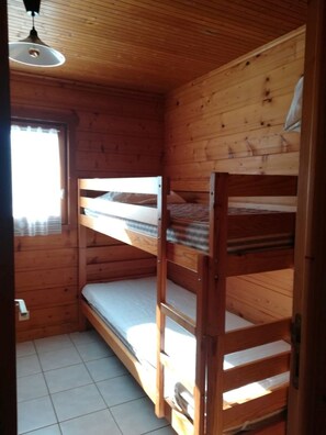 A wooden cabin room with bunk beds, a window with curtains, and a ceiling light. - In the Périgord Noir, between Sarlat and Montignac, comfortable chalet* in a peaceful setting (Saint-Geniès)