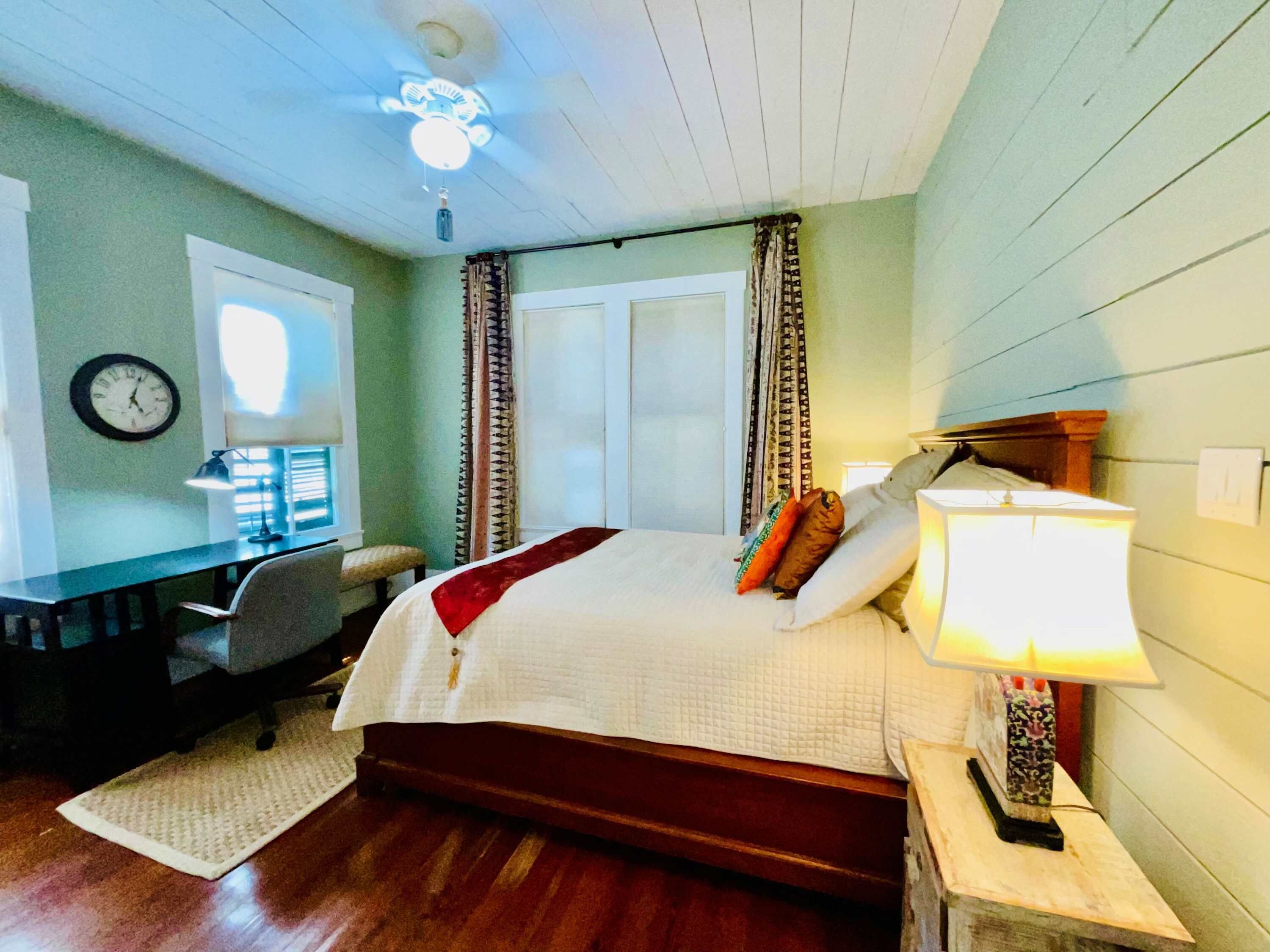 A bedroom with a bed, desk, chair, lamp, and a clock on the wall.