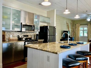 A kitchen with stainless steel appliances, a granite countertop, and a bar area with stools. - Verdant Red Door Retreat (Galveston)