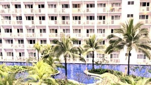 Un hôtel à plusieurs étages, doté de balcons et d’un espace piscine agrémenté de palmiers.