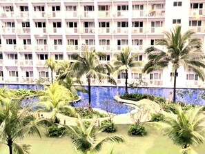 Ein Hotel mit mehreren Etagen, Balkonen und einem Poolbereich mit Palmen.