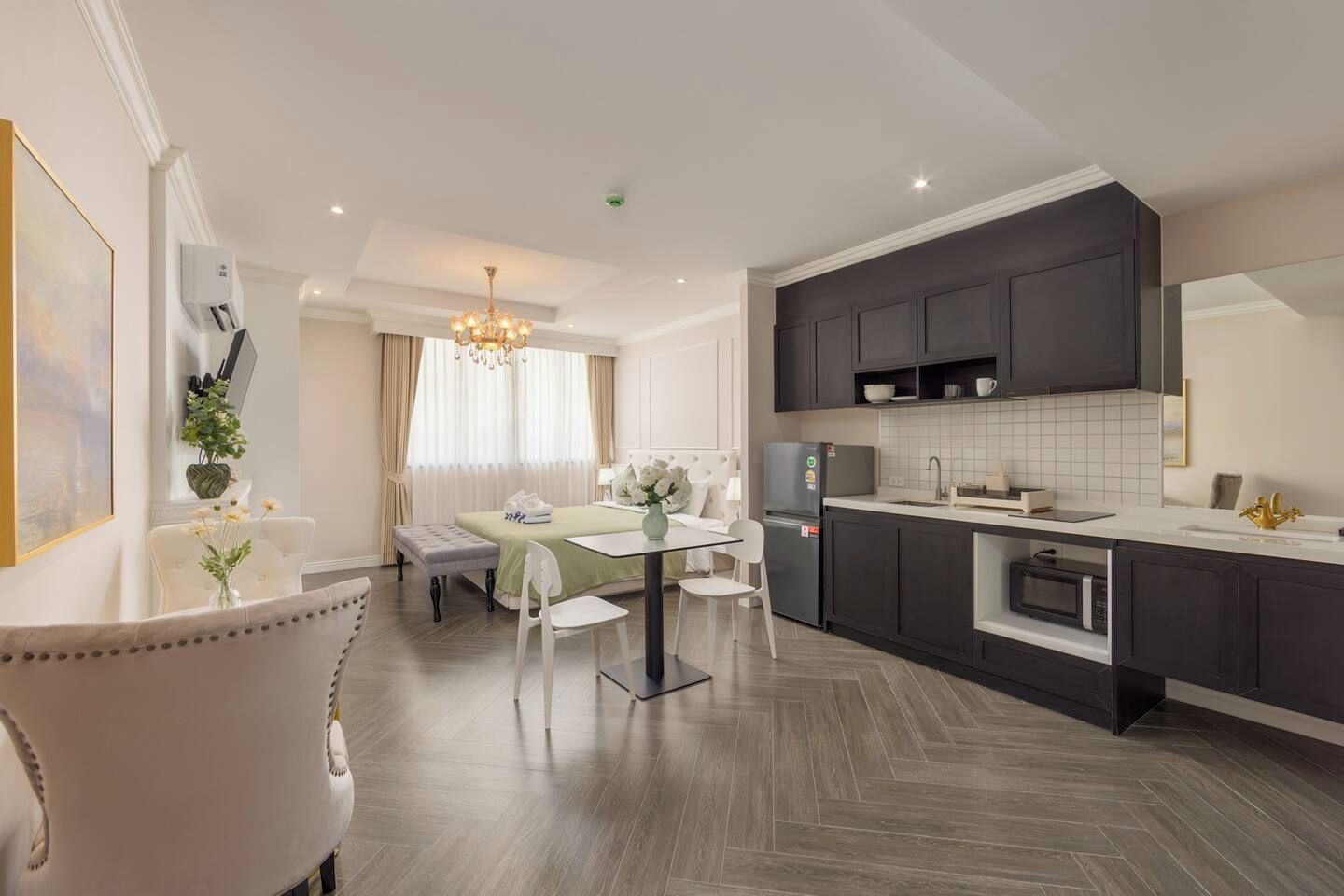 A modern hotel room with a dining area, kitchenette, and a large mirror.