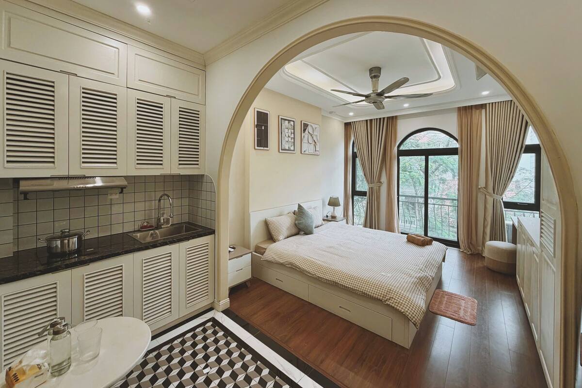 Un dormitorio con una cama grande, ventilador de techo, ventana con cortinas y vistas a la vegetación.