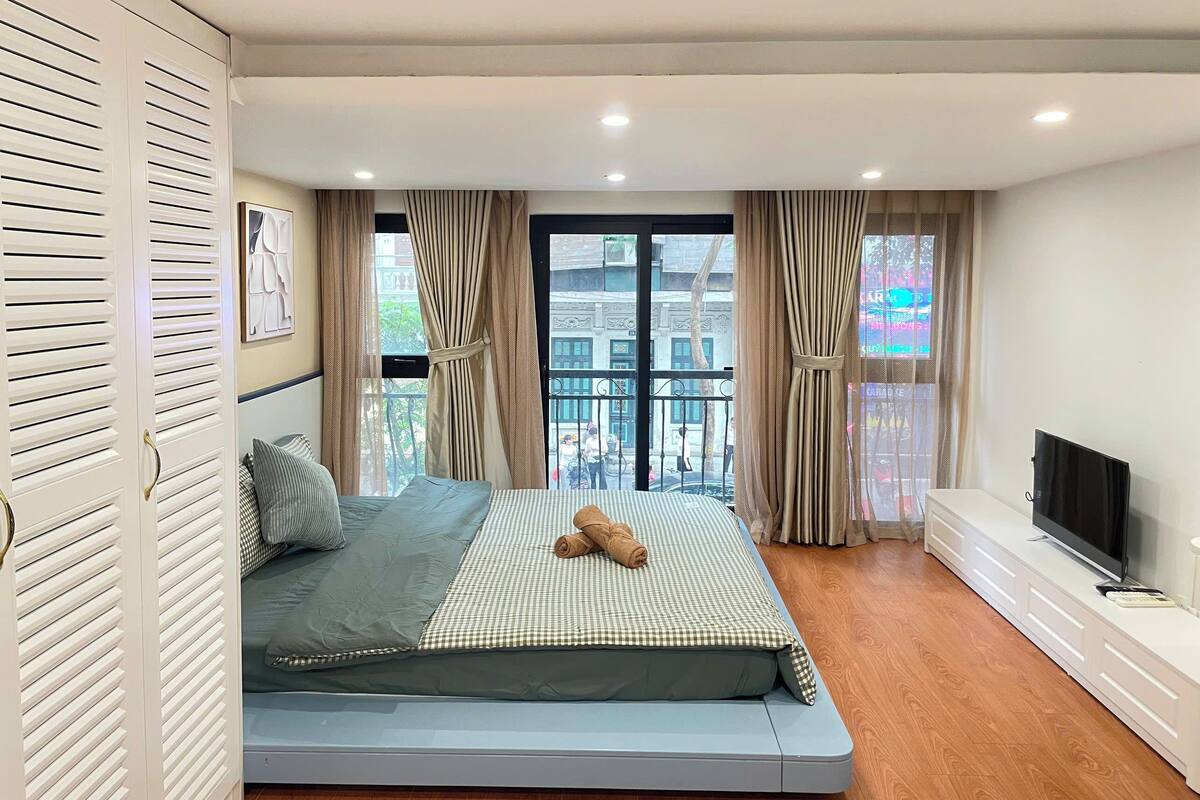 Un dormitorio con cama, cortinas, televisor y vistas al balcón.