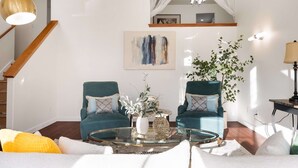 Un salon avec un escalier, deux fauteuils turquoise, une table basse en verre et une plante en pot.