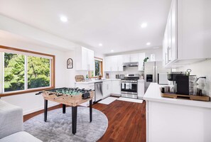A modern kitchen with white cabinets, a foosball table, and a large window with a view of greenery. - Private 3BR Greenbelt in Peaceful Lynnwood (Lynnwood)