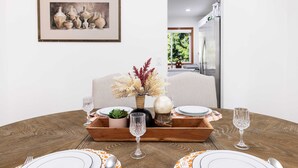 Une table à manger dressée avec des assiettes, des couverts et des verres, un vase contenant des fleurs séchées et un tableau encadré accroché au mur.