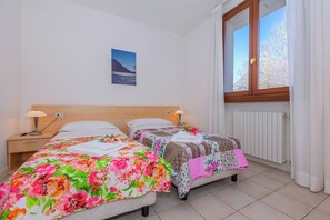 Ein Hotelzimmer mit zwei Betten, einem Fenster mit Vorhängen, einem Wandbild und einem Nachttisch mit Lampe.