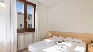 Hotellihuone, jossa on sänky, yöpöytä, verhoilla varustettu ikkuna ja patteri.