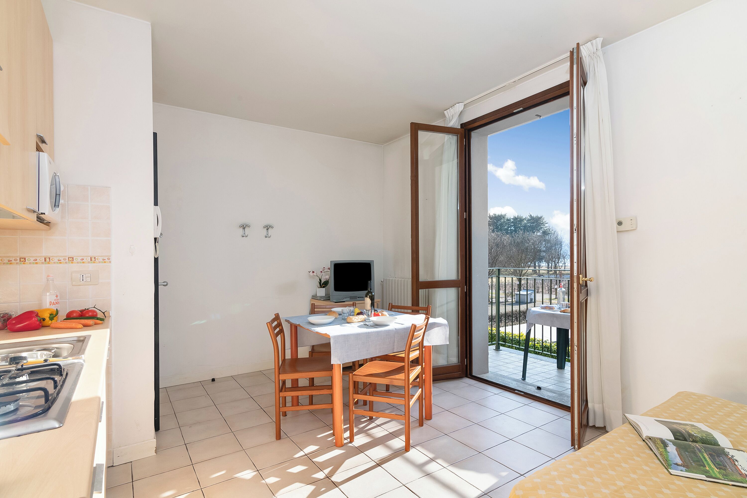 Een lichte kamer met een eettafel, stoelen, een televisie en een balkon met uitzicht.