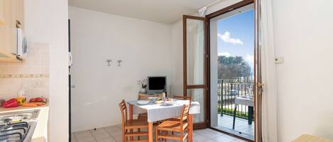 Une petite pièce lumineuse comprenant une table à manger, des chaises, un téléviseur et un balcon avec vue.