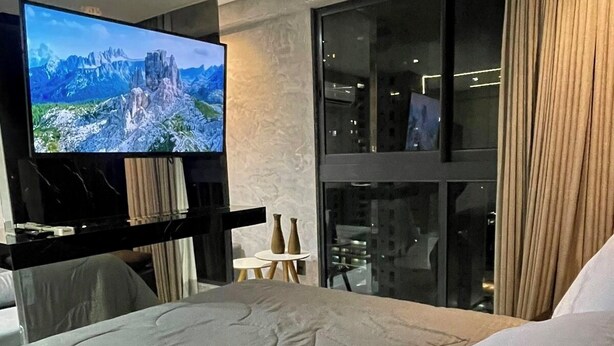 Een moderne hotelkamer met een groot bed, een flatscreen televisie, een glazen wand en uitzicht op de stad.