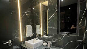 Een moderne badkamer met een zwart marmeren wastafelmeubel, een witte wasbak en een grote spiegel.