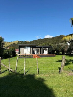 A modern two-story house with a large front lawn, a wooden deck, and a view of hills in the background.