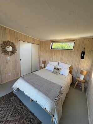 A bedroom with a bed, a window, a mirror, and a lamp.