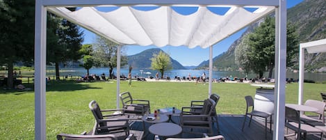 A wooden deck with outdoor seating and a white canopy overlooking a lake and mountains.