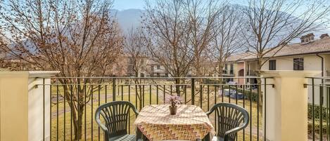Un balcon avec une table et des chaises, un pot de fleurs et une vue sur les arbres et les bâtiments.