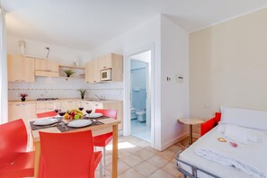 Eine moderne Küche mit Holdekor, ein Essbereich mit roten Stühlen und ein kleines Badezimmer, das durch eine offene Tür erkennbar ist.