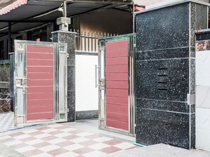 Un ingresso recintato con pavimento a scacchi, un cancello in metallo e una facciata di edificio con rivestimento scuro e maculato.