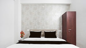 A bedroom with a bed, a nightstand, a vase with flowers, and a wooden wardrobe.