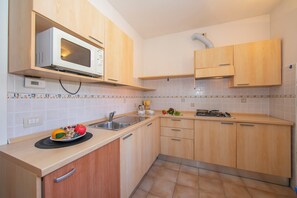 A modern kitchen with wooden cabinets, a microwave, a sink, and a stove. - Porto Letizia Como 4, Porlezza, Italy (Porlezza)