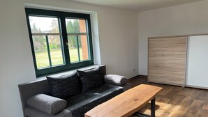 Una sala de estar moderna con un sofá gris, una mesa de centro de madera y un ventanal con vistas a un césped verde.