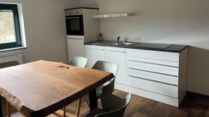 Cocina compacta con horno integrado, lavamanos y comedor con mesa y sillas.