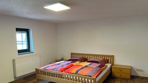 Un dormitorio con una cama de madera, una mesita de noche, una lámpara, un ventanal y un radiador.