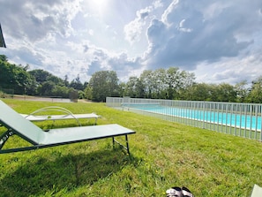 A swimming pool with a white fence, green grass, and a cloudy sky.