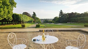 A garden with a table and chairs, a bottle of wine, and a view of a distant building. - Bed and breakfast at Château de Craon Swimming pool, tennis court, park Pdj included. (Craon)