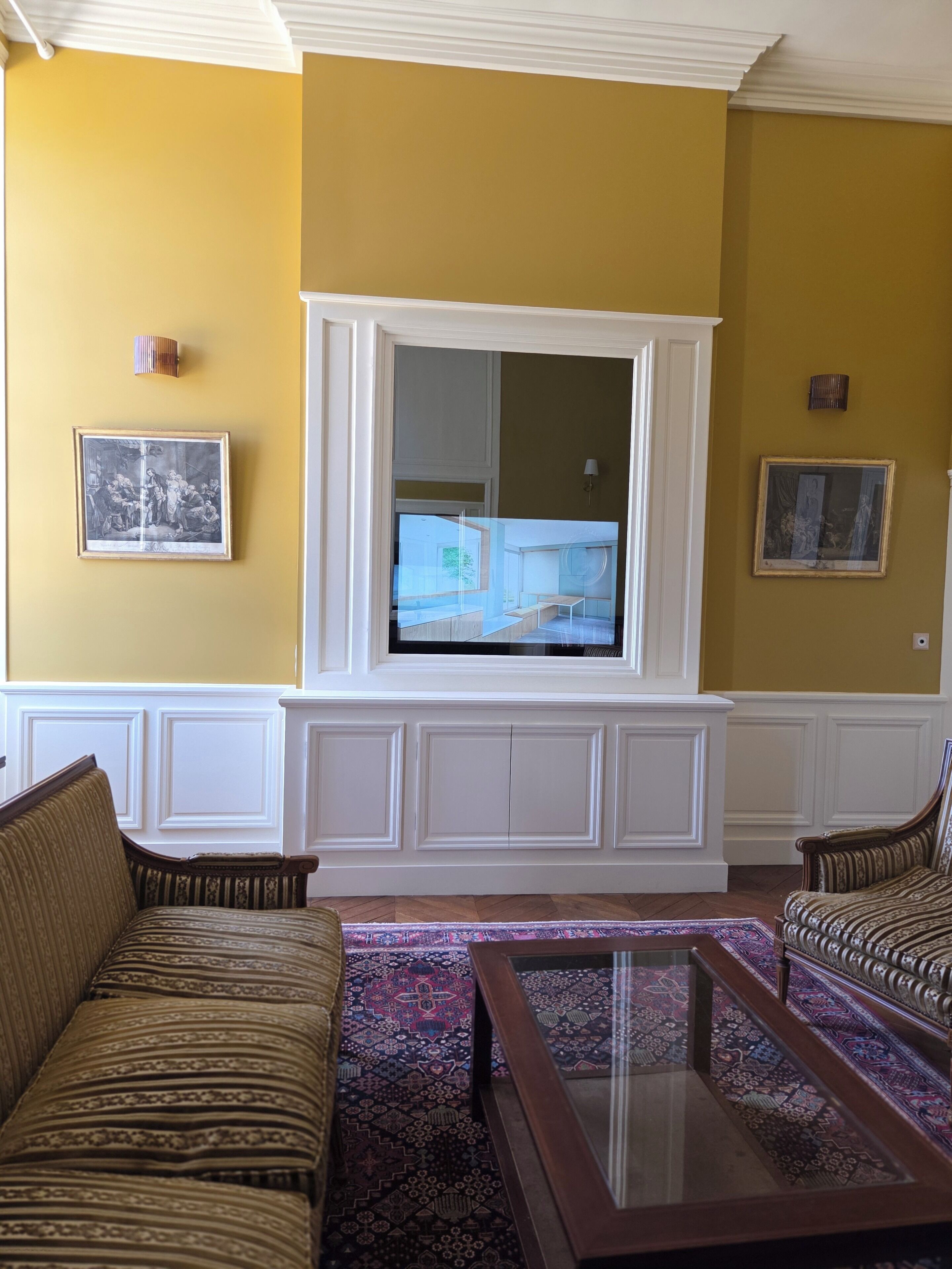 Een woonkamer met een grote tv die aan een witte paneel bevestigd is, twee gestreepte banken, een gestreept tapijt en twee ingelijste foto's aan de muur.